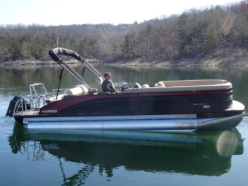 Slide: The Image of 2025 Harris Sunliner 250 pontoon boat on a calm lake with wooded shoreline. - 1