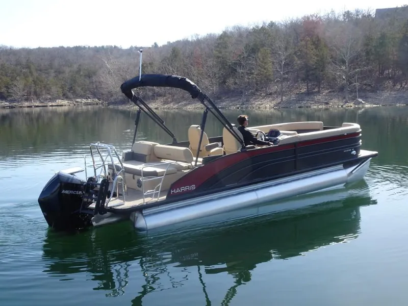 Slide: The Image of 2025 Harris Sunliner 250 pontoon boat cruising on a calm lake with scenic forest backdrop. - 2