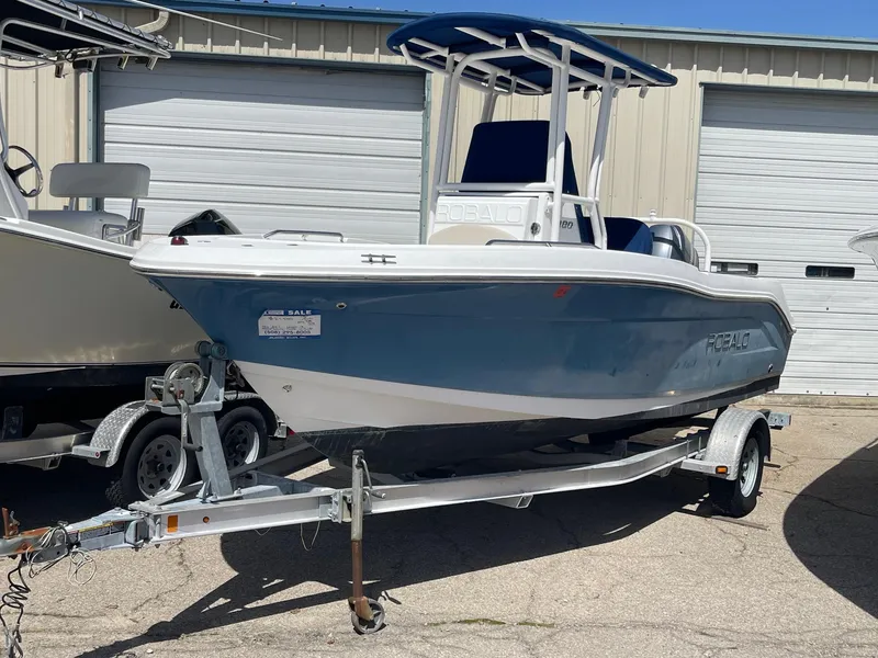 Slide: The Image of 2012 Robalo 180 CC boat on trailer, blue and white, parked outdoors. - 0