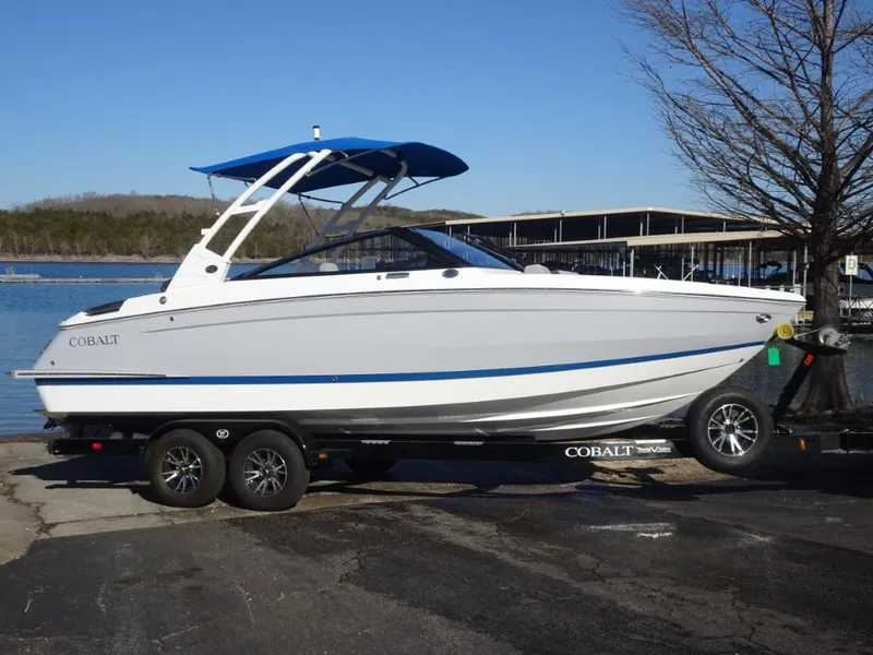 Slide: The Image of 2025 Cobalt R4 boat on trailer by a lake, featuring sleek design and blue accents. - 2