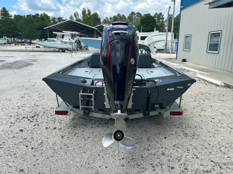 Slide: The Image of 2019 Triton 18 TX boat with outboard motor, parked on gravel near a building. - 17