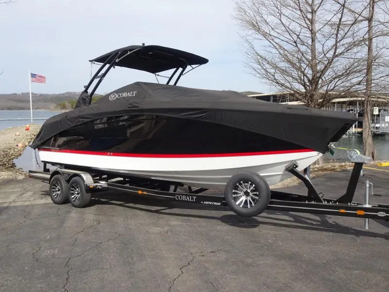 Slide: The Image of 2025 Cobalt R8 boat on trailer, covered, near a lake with American flag. - 24