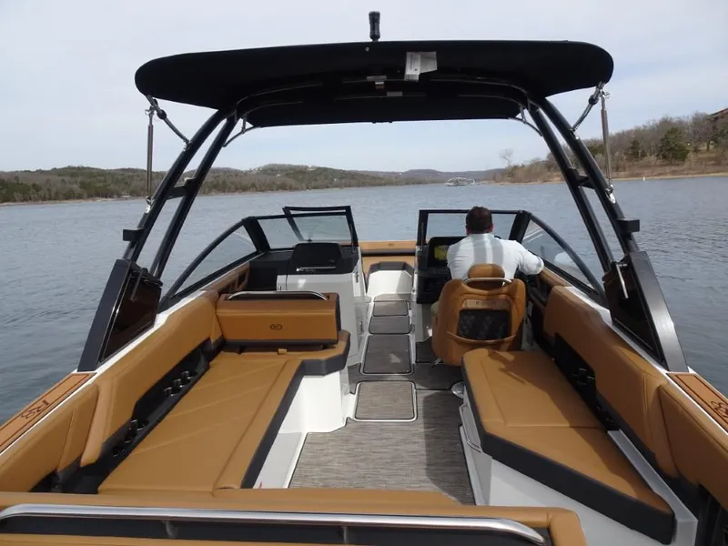 Slide: The Image of 2025 Cobalt R8 boat interior with tan seating, black canopy, and driver on a calm lake. - 7