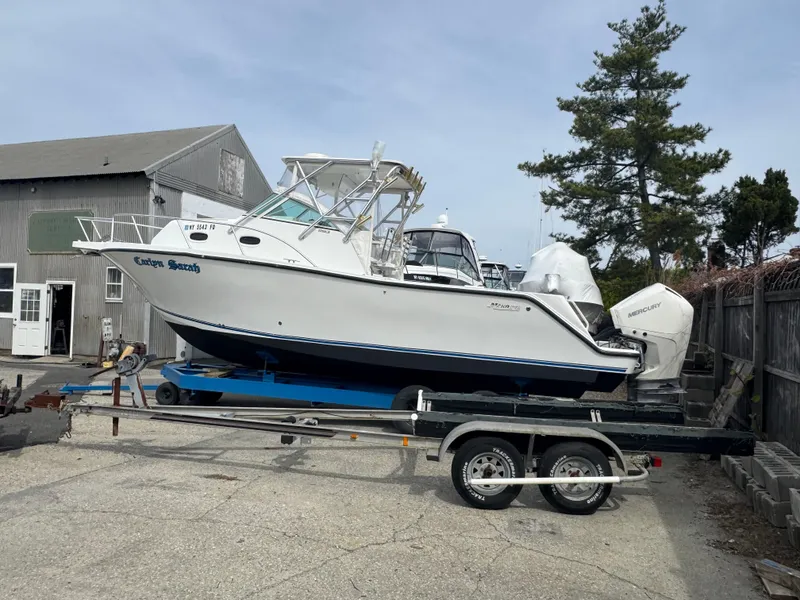 Slide: The Image of 2001 Mako 293 Walkaround boat on trailer, parked outdoors near a wooden building. - 0