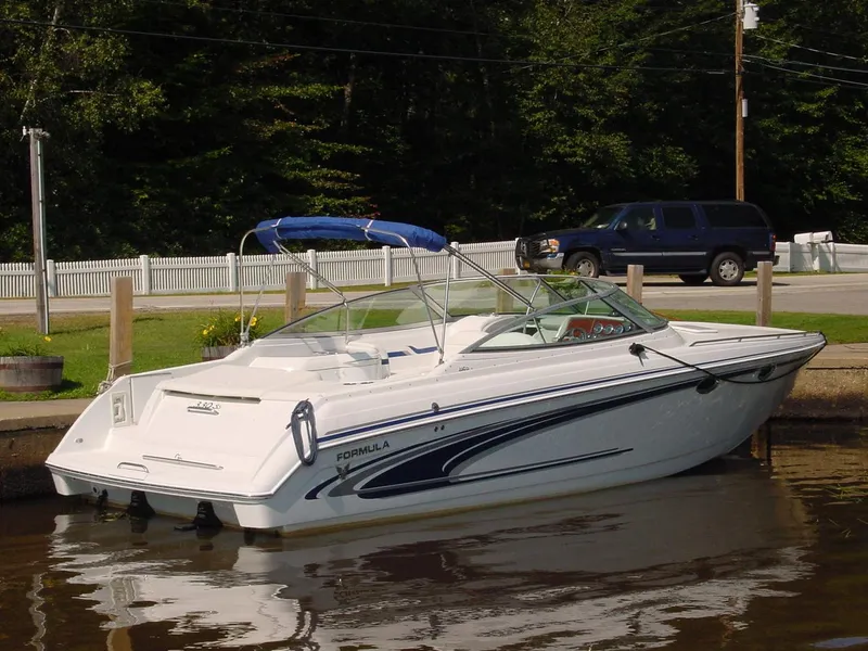 The Image of 2004 Formula 330 Sun Sport boat docked by a lakeside with trees and a parked SUV. - 0