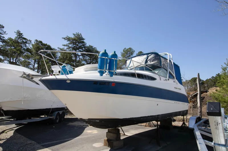 The Image of 2007 Bayliner 245 Cierra boat on dry dock, surrounded by trees and clear sky. - 0