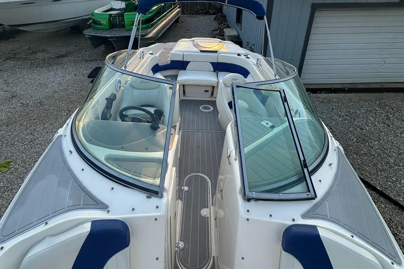 Slide: The Image of 2006 Rinker 262 Captiva Bowrider with blue and white interior, docked on gravel. - 20