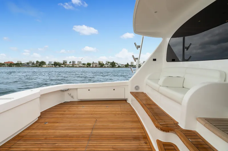 Slide: The Image of 2025 Viking 58 Convertible yacht deck with wooden flooring and white seating, overlooking calm waters. - 30