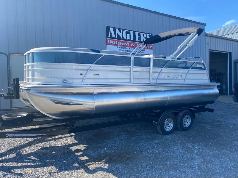 Slide: The Image of 2024 Trifecta 22CL2 LE pontoon boat on trailer outside Anglers Outpost & Marine. - 1