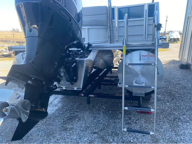 Slide: The Image of 2024 Trifecta 22CL2 LE pontoon boat with motor and ladder, parked on gravel. - 28