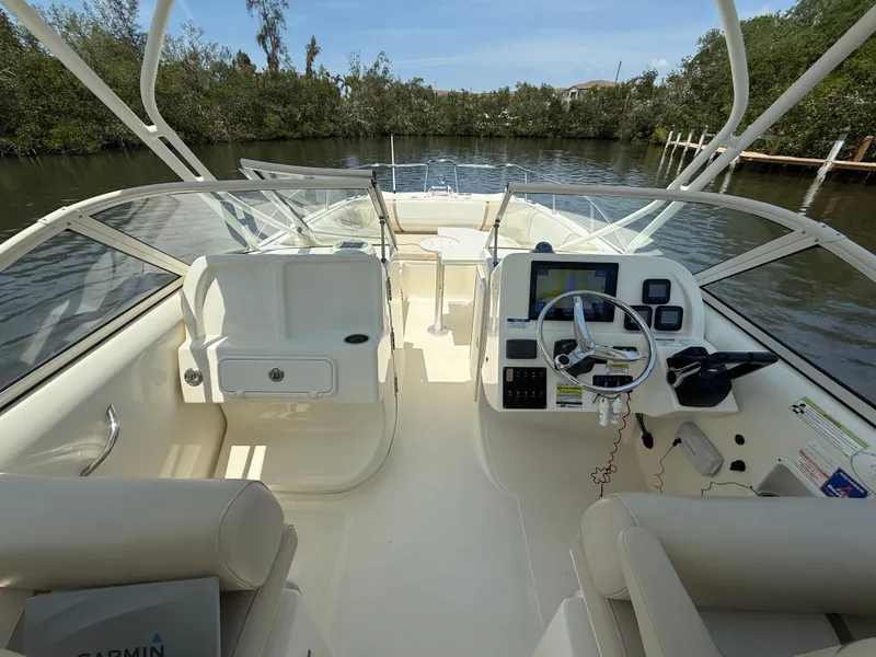 Slide: The Image of 2015 World Cat 255 DC boat interior with steering console and seating, on a calm waterway. - 13