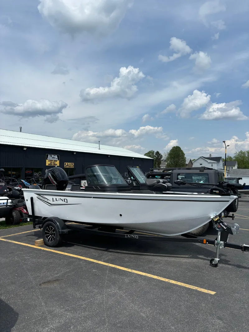 The Image of 2025 Lund 1650 Rebel XL Sport boat on trailer in parking lot under cloudy sky. - 1