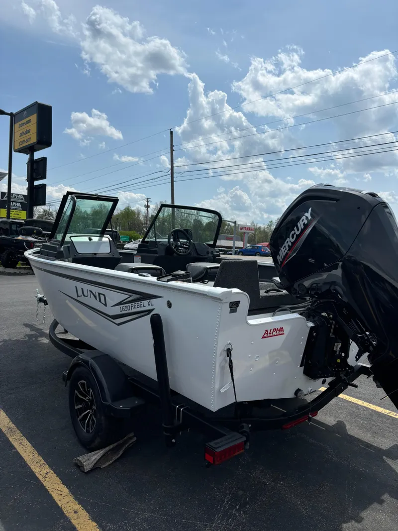 Slide: The Image of 2025 Lund 1650 Rebel XL Sport boat with Mercury engine, parked outdoors under a cloudy sky. - 5