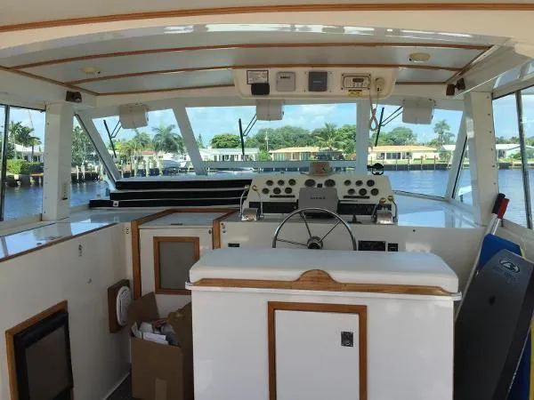 Slide: The Image of 1987 Bertram Motoryacht helm with steering wheel, control panel, and waterfront view. - 5