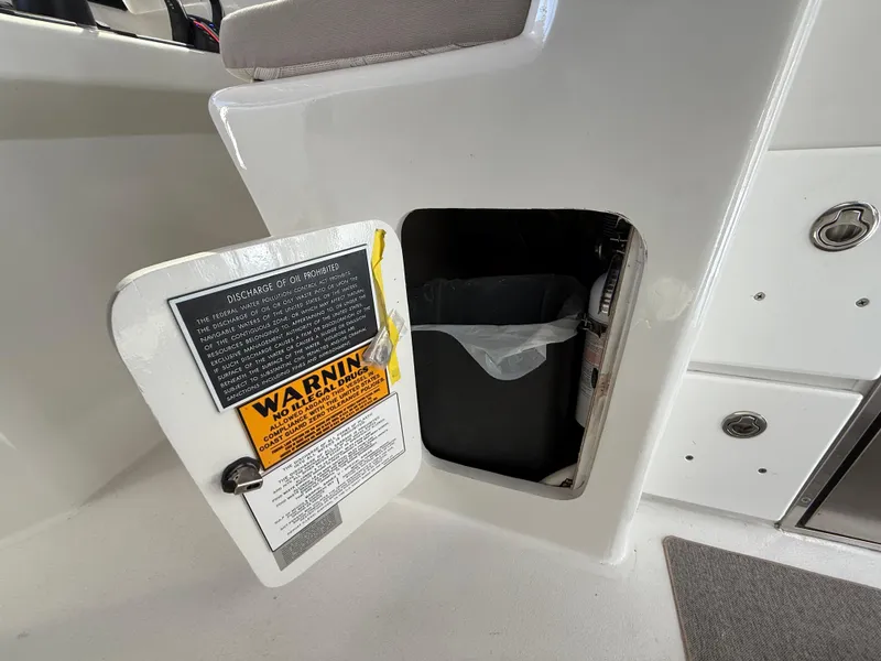 Slide: The Image of 2023 Millennium Marine NuWave 37 boat storage compartment with warning label and trash bin. - 33