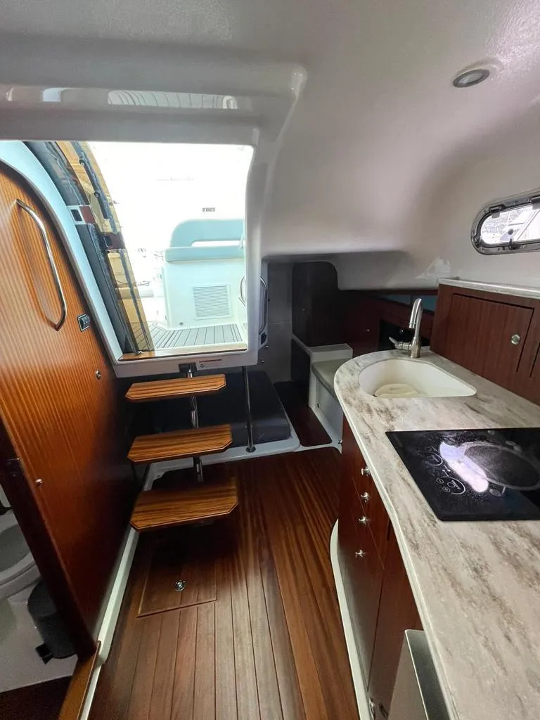 Slide: The Image of 2019 Pursuit OS 385 Offshore interior with wooden flooring, kitchenette, and steps leading to deck. - 24