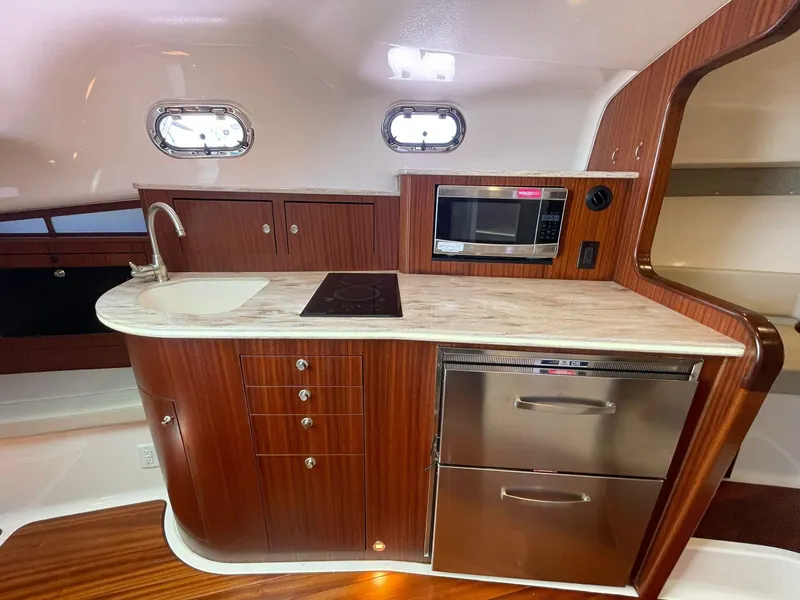 Slide: The Image of 2019 Pursuit OS 385 Offshore yacht kitchen with wood cabinetry, sink, stove, microwave, and stainless steel appliances. - 26