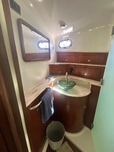 Slide: The Image of 2019 Pursuit OS 385 Offshore bathroom with wood cabinetry, glass sink, and porthole windows. - 29