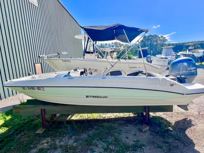 Slide: The Image of 2017 Stingray 182 SC boat with canopy, parked outdoors near other boats. - 3