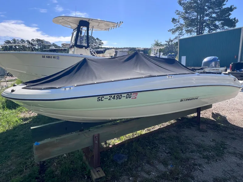 Slide: The Image of 2017 Stingray 182 SC boat with cover, parked on a wooden stand outdoors. - 4