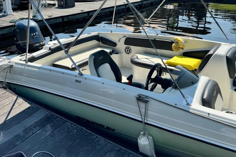 Slide: The Image of 2017 Stingray 182 SC boat docked, featuring seating and steering wheel, with water in the background. - 8