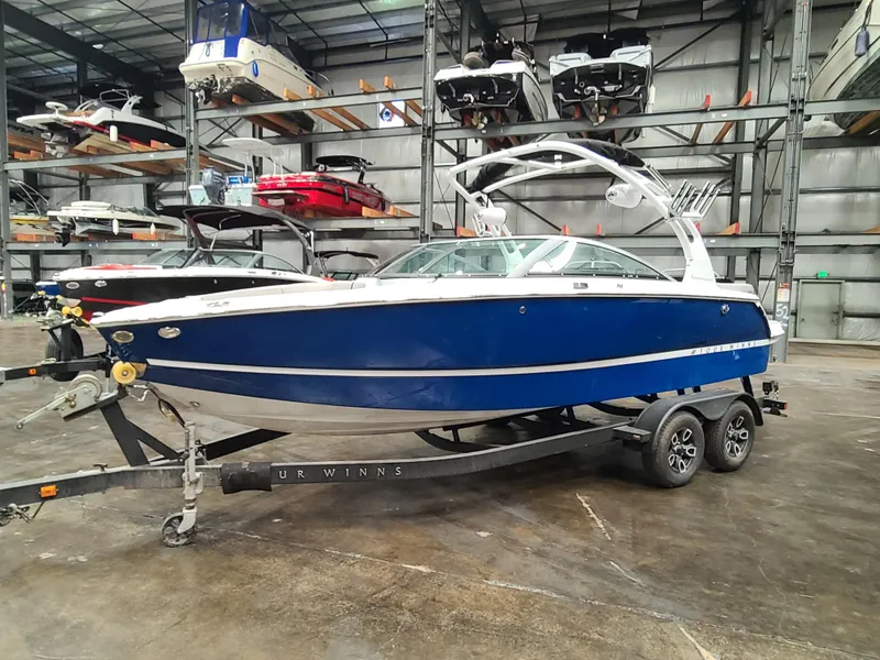 Slide: The Image of 2023 Four Winns H2 boat in storage, blue hull, on a trailer. - 2