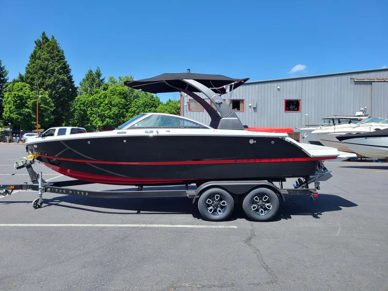 Slide: The Image of 2023 Four Winns H2 Surf boat on trailer, black and red design, parked outdoors. - 1