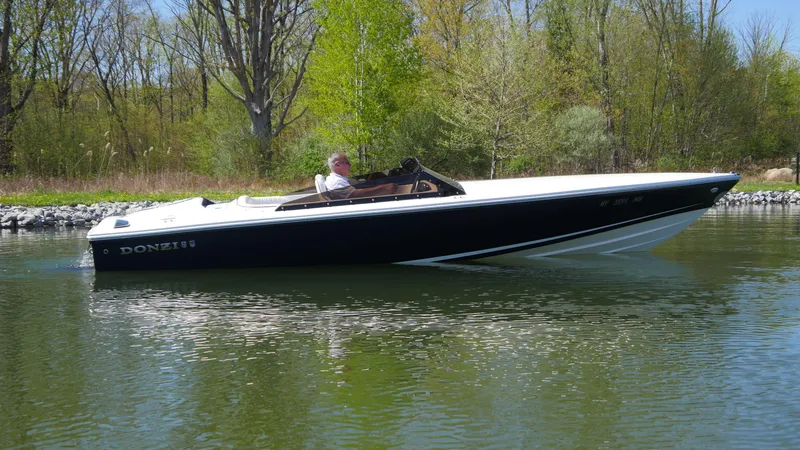 Slide: The Image of 2022 Donzi 22 Classic boat cruising on a calm lake with lush greenery. - 19