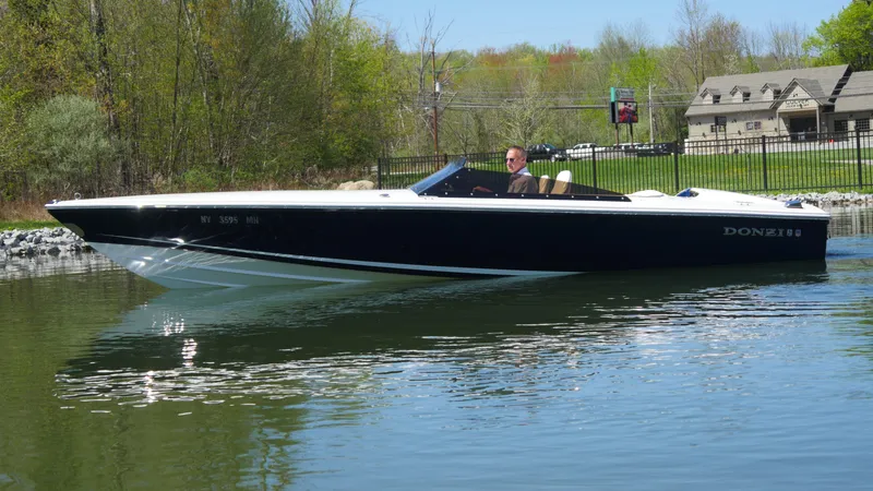 Slide: The Image of 2022 Donzi 22 Classic boat cruising on a calm lake near a wooded shoreline. - 22