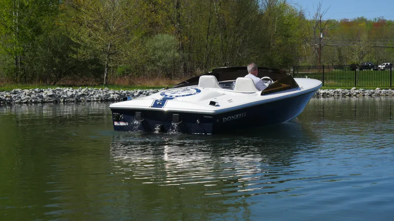 Slide: The Image of 2022 Donzi 22 Classic boat cruising on a calm lake with lush greenery. - 3