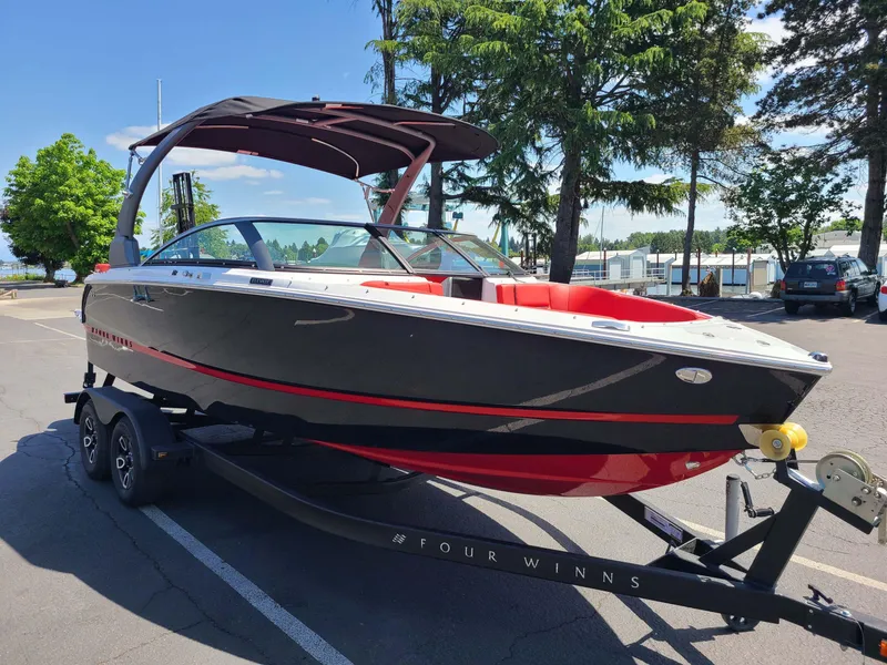 Slide: The Image of 2023 Four Winns H2 Surf boat on trailer, black and red design, parked outdoors. - 2