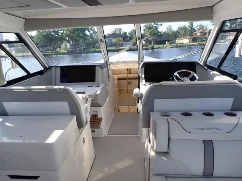 Slide: The Image of Interior of 2023 Regal LX36 boat with modern seating and steering, overlooking a scenic waterfront. - 19