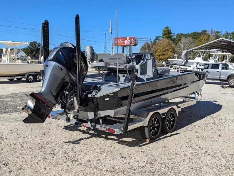 Slide: The Image of 2025 Xpress X23B Lounge boat on trailer, parked outdoors under clear blue sky. - 2