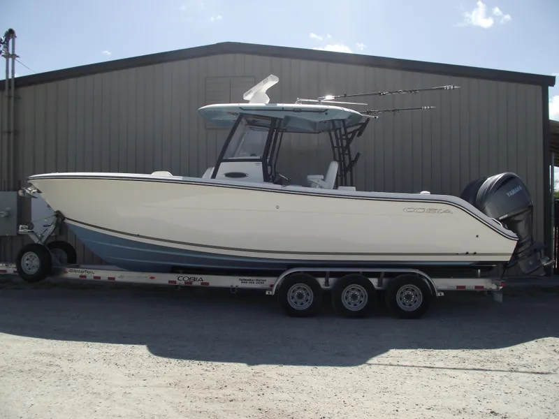 Slide: The Image of 2021 Cobia 301 Center Console boat on trailer, parked outside a metal building. - 0
