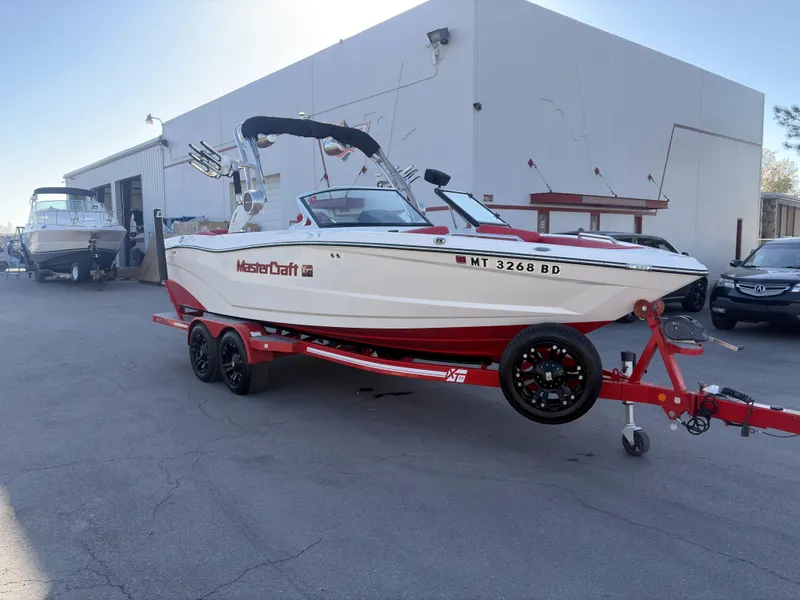 Slide: The Image of 2018 MasterCraft XT23 boat on red trailer parked outside a building. - 1