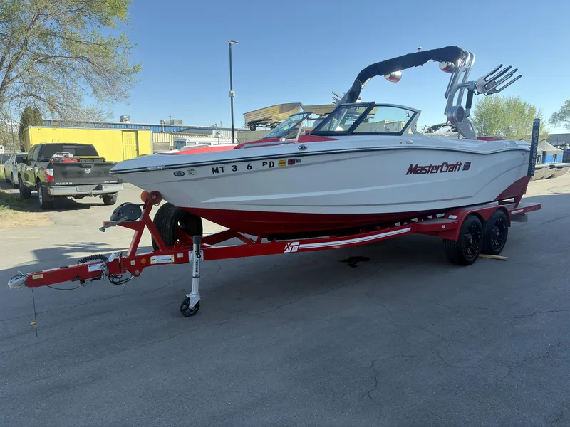 Slide: The Image of 2018 MasterCraft XT23 boat on red trailer, parked outdoors. - 3