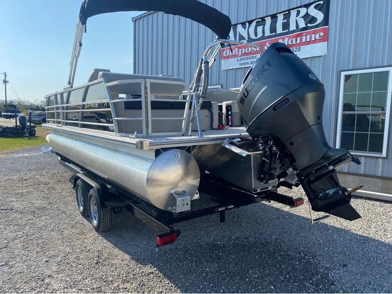 Slide: The Image of 2025 Trifecta 24 UL LE pontoon boat with Suzuki outboard motor, parked outside marine shop. - 24