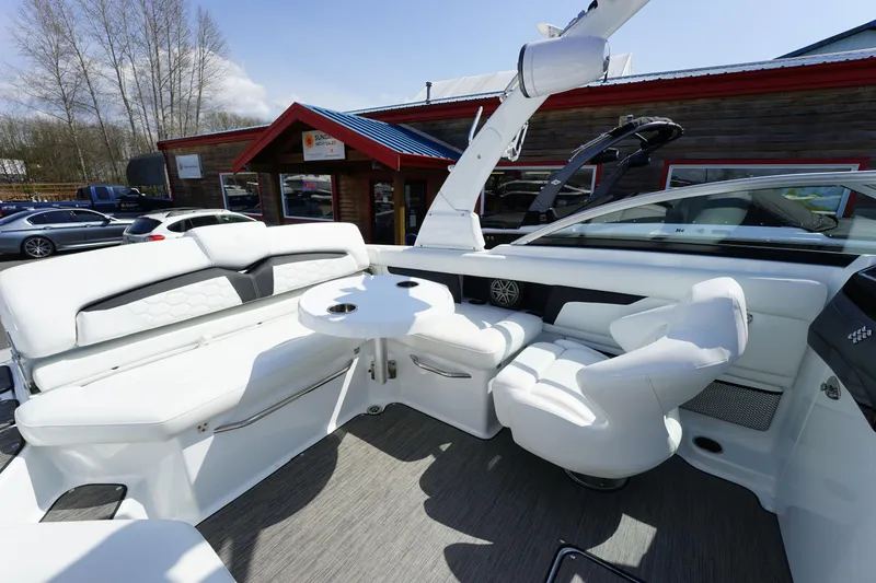 Slide: The Image of 2023 Four Winns HD3 Surf boat interior with white seating and table, parked outdoors. - 21