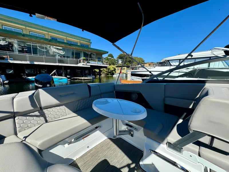 Slide: The Image of 2023 Four Winns H2 boat interior with seating and table, docked near waterfront buildings. - 11