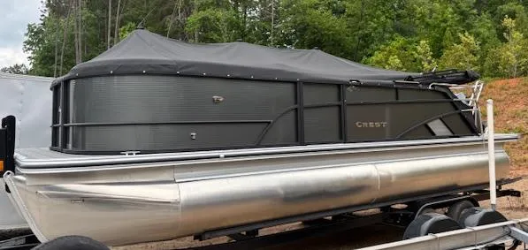 Slide: The Image of 2025 Crest Classic 220 pontoon boat with cover on trailer, surrounded by trees. - 10