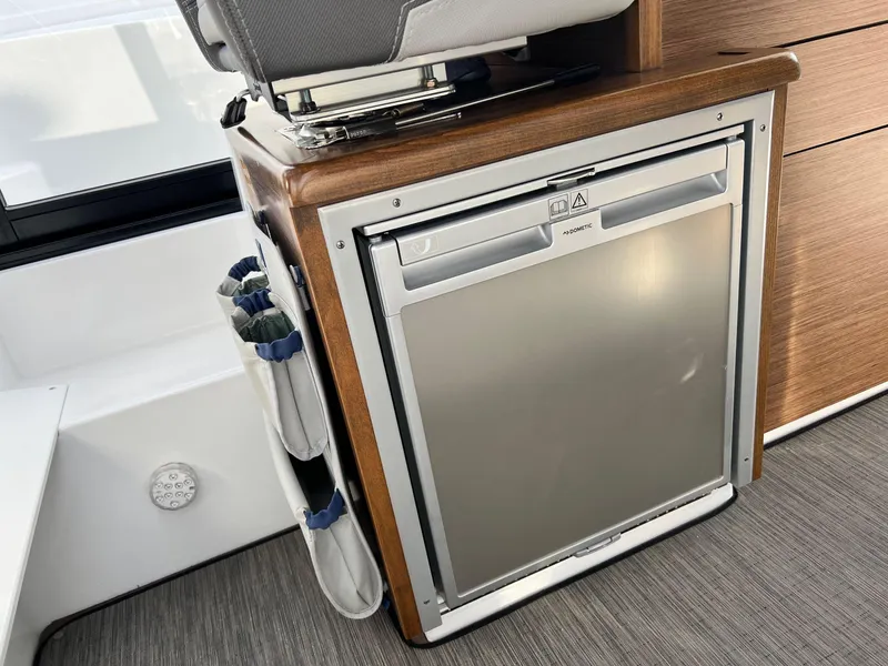 Slide: The Image of 2023 Jeanneau NC 895 interior featuring a compact, built-in refrigerator with wooden accents. - 11