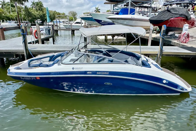 Slide: The Image of 2011 Yamaha Boats 242 Limited in marina, blue and white, with canopy, docked near other boats. - 27