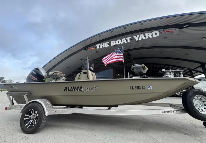 Slide: The Image of 2019 Alumacraft 18 Bay boat on trailer, displayed at The Boat Yard with American flag. - 2