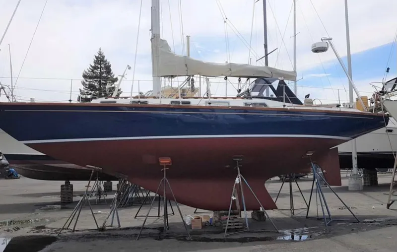 Slide: The Image of 1984 Ohlson 38 sailboat on stands, blue hull, white deck, in a boatyard. - 3