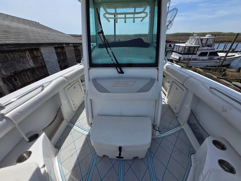 Slide: The Image of 2013 Boston Whaler 280 Outrage boat interior with seating and storage, docked near wooden buildings. - 3