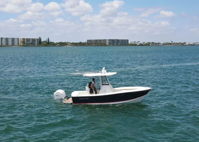 Slide: The Image of 2024 Regulator 23 boat cruising on a sunny day with buildings in the background. - 2