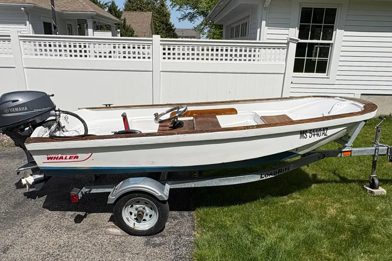 Slide: The Image of 1984 Boston Whaler 11 boat on trailer, parked in driveway, with Yamaha outboard motor. - 0