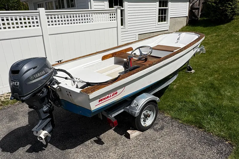 Slide: The Image of 1984 Boston Whaler 11 boat with Yamaha motor on a trailer, parked in a driveway. - 1
