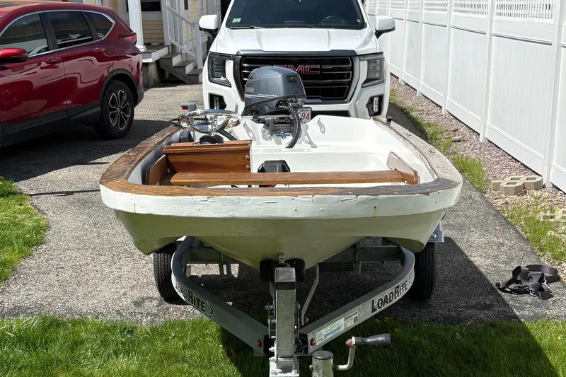 Slide: The Image of 1984 Boston Whaler 11 boat on trailer, parked in driveway with vehicles nearby. - 4