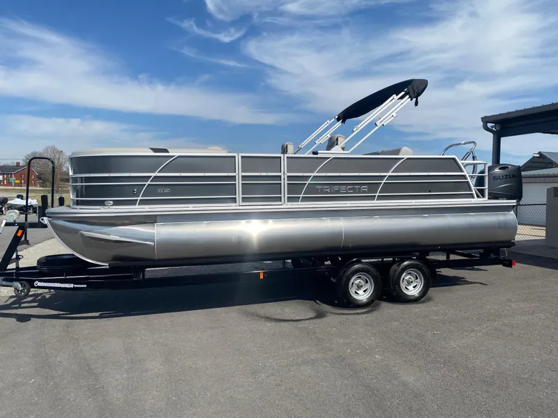 Slide: The Image of 2025 Trifecta LE Series 22UL pontoon boat on trailer, parked outdoors under blue sky. - 1